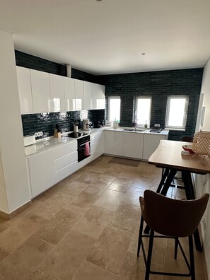 A modern kitchen with white cabinets, a black backsplash, and a dining area with a wooden table and chairs.