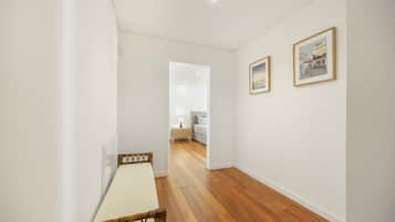 A hallway with a wooden floor, a bed with a white headboard, and two framed pictures on the wall.