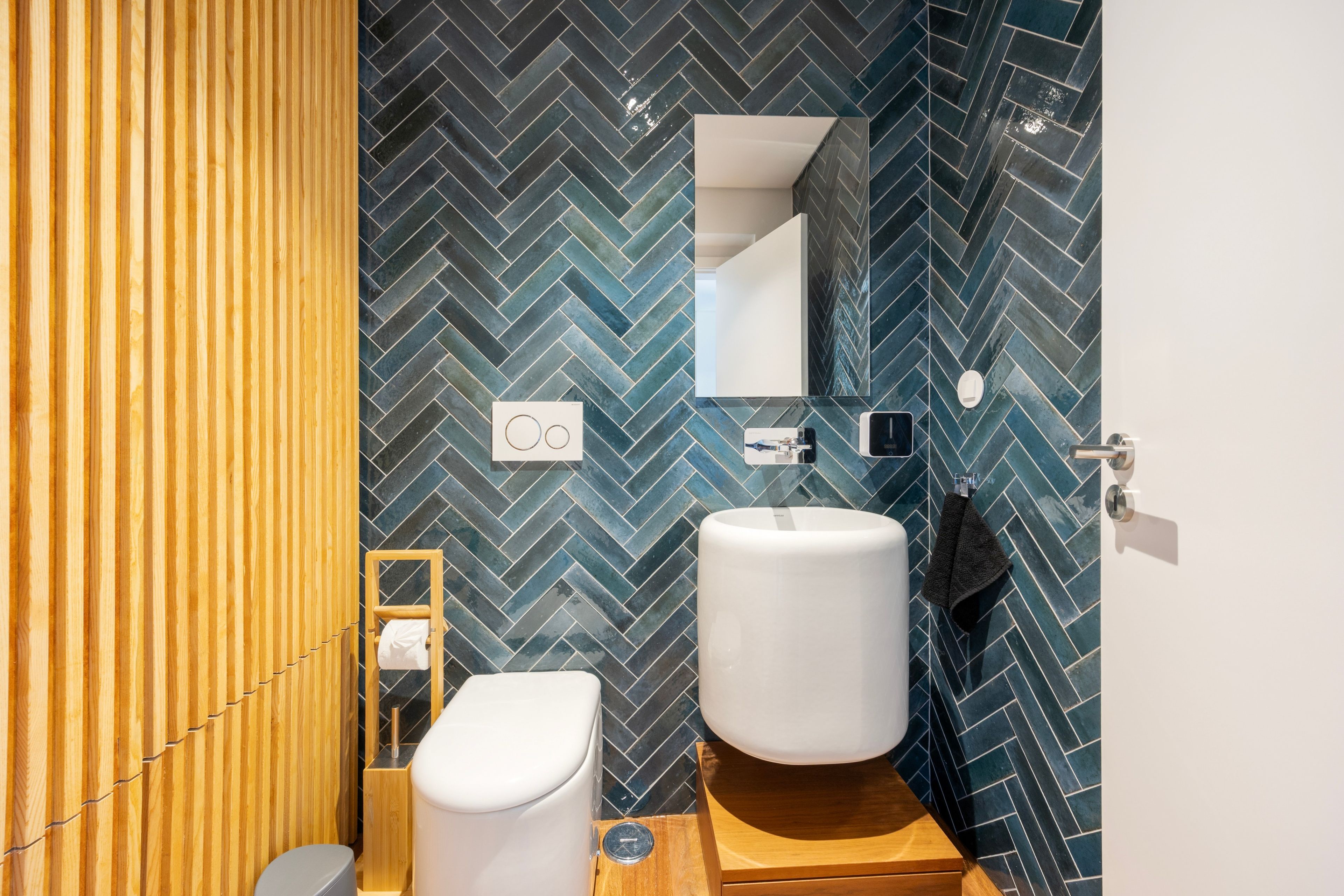 Un baño moderno con un patrón de baldosas de espiga, una partición de madera, un inodoro, un lavabo y un espejo.