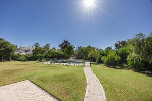 A sunny outdoor area with a paved walkway leading to a pool, surrounded by greenery and a clear sky. - Villa Casa Lagartixa — your Algarve retreat (Alvor)