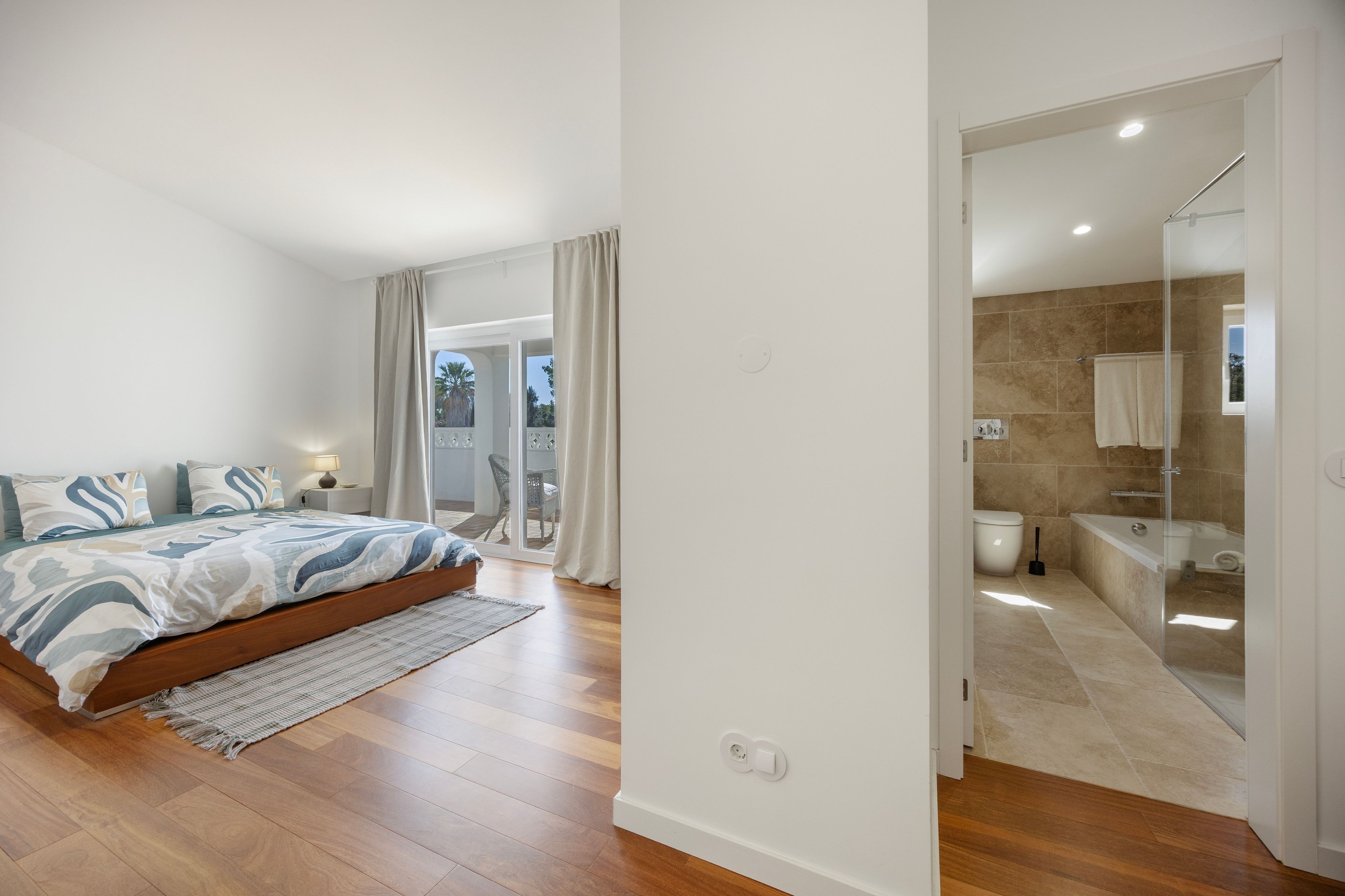 Une chambre à coucher avec un lit, une table de chevet et une vue sur un balcon.