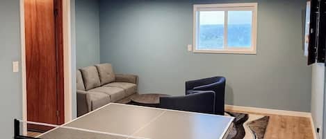 Una habitación con mesa de ping pong, sofá, sillón, ventana con vistas y puerta.