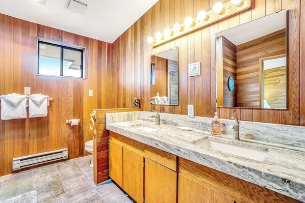 Un baño con paneles de madera, un espejo grande, tocador con encimera de mármol y un perchero para toallas.