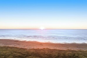 Ein Strand mit blauem Himmel und tiefstehender Sonne, was auf Sonnenaufgang oder Sonnenuntergang hindeutet.