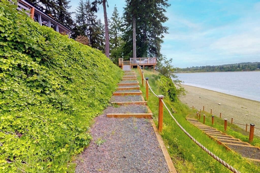A pathway leading to a wooden deck overlooking a beach with a body of water in the background.