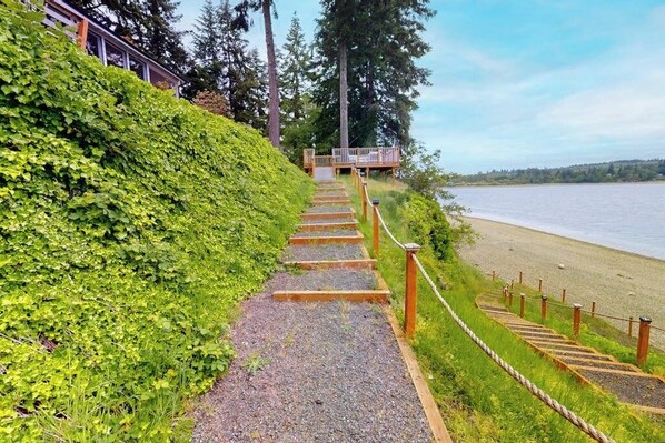 A pathway leading to a wooden deck overlooking a beach with a body of water in the background. - Waterfront home with hot tub, pool table, firepit (Vashon)