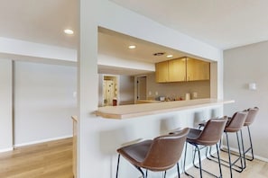 A modern kitchen with a bar area, wooden cabinets, and four bar stools. - Waterfront home with hot tub, pool table, firepit (Vashon)
