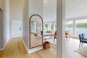 A spacious room with a large mirror, wooden flooring, a cozy seating area with a sofa and chairs, and a view of a lake through large windows. - Waterfront home with hot tub, pool table, firepit (Vashon)
