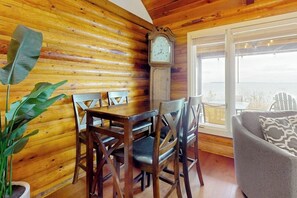 Ein Holzhütten-Interieur mit einem Esstisch, Stühlen, einer Uhr und Blick durch ein Fenster.