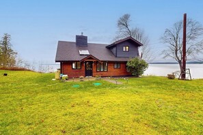 A two-story log cabin with a dark roof, a chimney, and a front porch with a door.