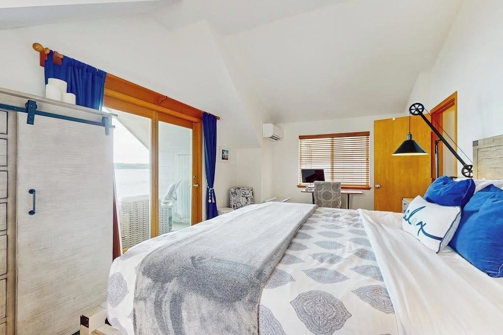 A bedroom with a bed, a desk, a chair, and a window with blinds.