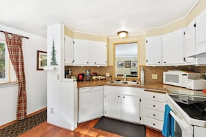 A compact kitchen with white cabinets, a dishwasher, a microwave, and a stove. - Secluded 3BR with hot tub, firepit & deck (Gold Bar)