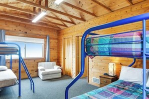 Ein Zimmer in einer Holzhütte mit Etagenbetten, einem Sessel, einem Nachttisch und einem Fenster.