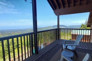 A covered outdoor area with a wooden deck, two chairs, and a view of a mountainous landscape. - Spacious 2BR Oceanview Dog Friendly - Hot Tub (Port Angeles)