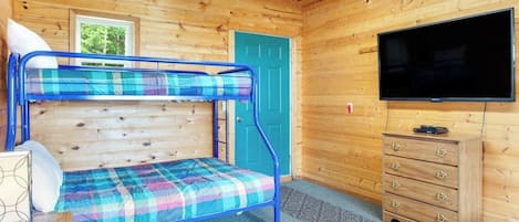 Una habitación de cabaña de madera con literas, un televisor y un aparador.