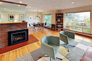 A modern living room with a fireplace, a dining area, and a bookshelf. - Modern 3BR Bayview - Elevator - Deck - Washer Dryer (Seattle)