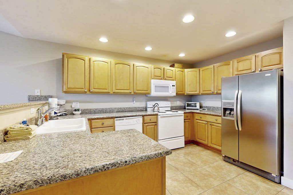 A kitchen with granite countertops, wooden cabinets, a stainless steel refrigerator, a microwave, a stove, and a dishwasher.