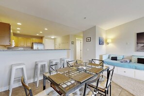 A modern kitchen with a dining area, white cabinetry, and a seating area with a sofa and cushions. - 2BR Oceanfront 3rd-Floor - Deck - (Westport)