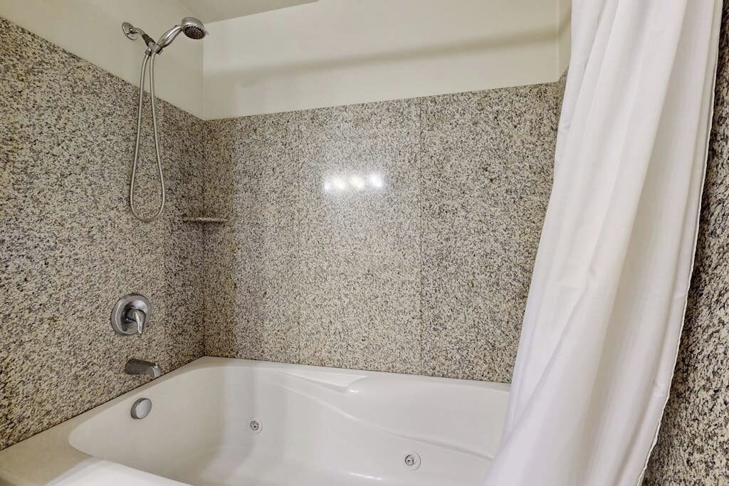 A bathroom with a granite-tiled wall, a white bathtub, and a showerhead.