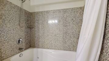 A bathroom with a granite-tiled wall, a white bathtub, and a showerhead.