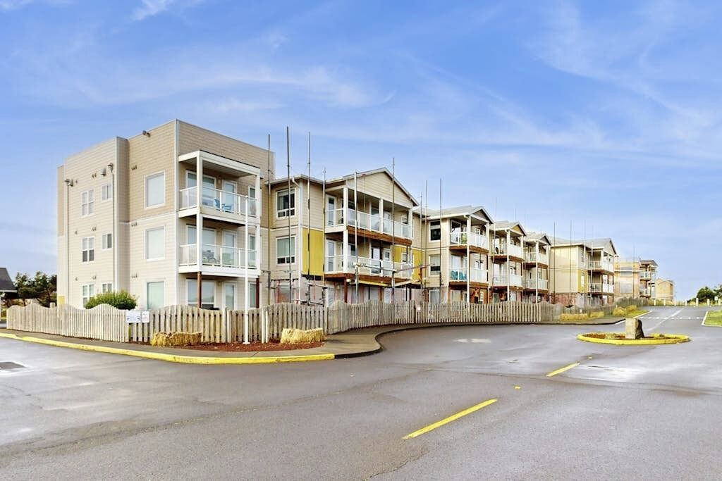 Una hilera de edificios residenciales de varios pisos con balcones, un estacionamiento cercado y un cielo despejado.