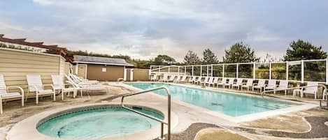 Ein Pool mit Liegestühlen und einer kleinen Whirlwanne, umgeben von einer Sonnenterrasse.