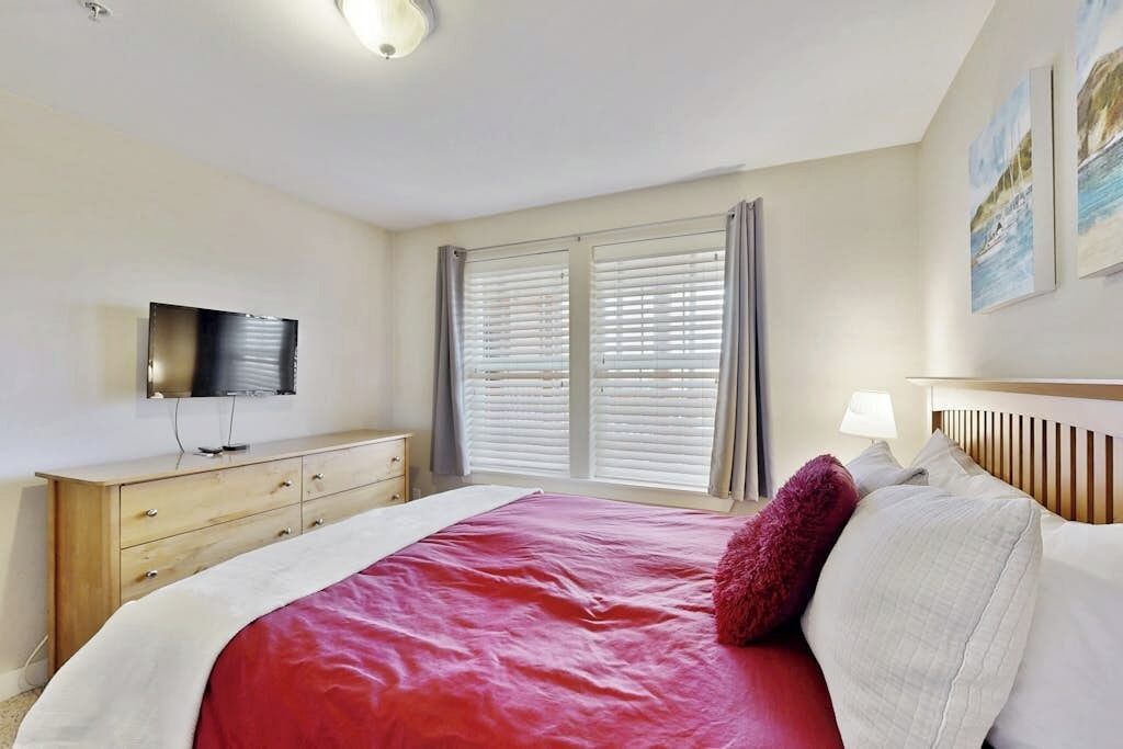 Een hotelkamer met een bed, een televisie op een dressoir en een raam met jaloezieën.