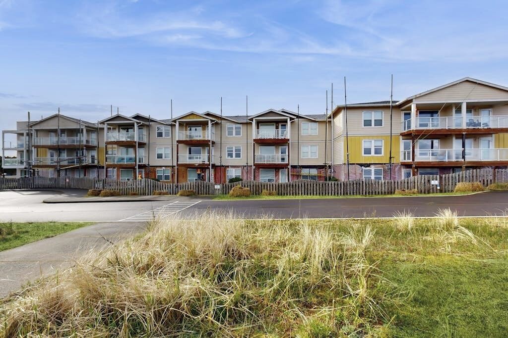 Una fila di edifici residenziali a più piani con balconi, un parcheggio e un'area verde in primo piano.