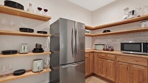 Una cocina moderna con un refrigerador de acero inoxidable, estantes de madera y un microondas.