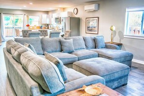 A modern living room with a sectional sofa, a wooden coffee table, and a kitchen in the background. - 3BR - Deck - Firepit - Washer Dryer (Westport)