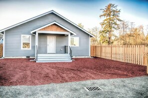 A single-story house with a front porch, a wooden fence, and a red mulch ground cover. - 3BR - Deck - Firepit - Washer Dryer (Westport)