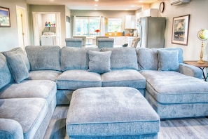 A modern living room with a sectional sofa, a dining area, and a kitchen in the background. - 3BR - Deck - Firepit - Washer Dryer (Westport)