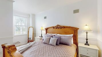 A neatly arranged bedroom with a wooden bed, two bedside tables with lamps, a mirror, and a window with blinds.
