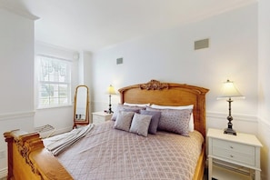 A neatly arranged bedroom with a wooden bed, two bedside tables with lamps, a mirror, and a window with blinds. - Steps to Beach 1BR Oceanfront Judith Ann Inn (Ocean Shores)