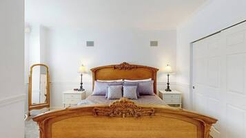Un dormitorio con una cama de madera, dos mesitas de noche con lámparas, un espejo y una puerta blanca.