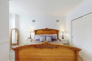Un dormitorio con una cama de madera, dos mesitas de noche con lámparas, un espejo y una puerta blanca.