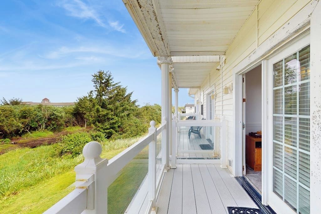 Een overdekt terras met een witte balustrade, een glazen deur naar binnen en uitzicht op een groen landschap.