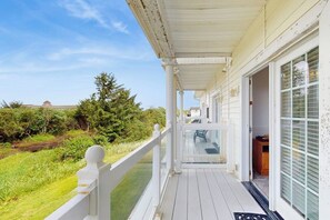 Een overdekt terras met een witte balustrade, een glazen deur naar binnen en uitzicht op een groen landschap.