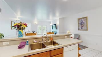 A modern kitchen with a double sink, wooden cabinets, a white countertop, and a vase of flowers on the counter.