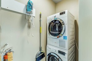 A laundry area with stacked washing machines, a broom, and a fire extinguisher.