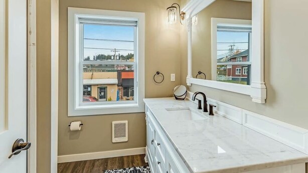 A bathroom with a double vanity, a large mirror, and a window providing a view of buildings outside. - Front Street Suite Poulsbo (Poulsbo)