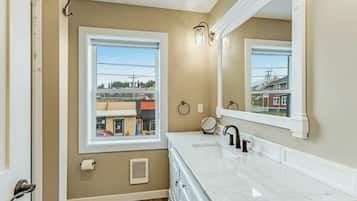 A bathroom with a double vanity, a large mirror, and a window providing a view of buildings outside.
