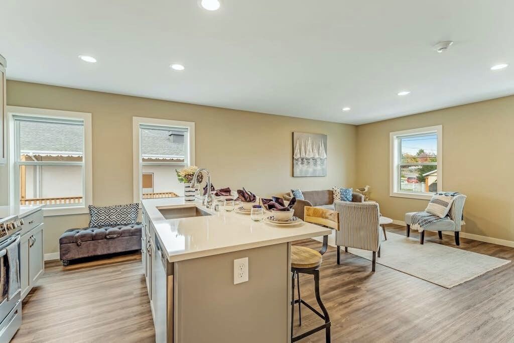 A modern kitchen with a central island, a dining area with a sofa, and a view of the outdoors through large windows.