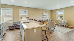 A modern kitchen with a central island, a dining area with a sofa, and a view of the outdoors through large windows. - Front Street Suite Poulsbo (Poulsbo)