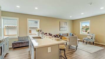 A modern kitchen with a central island, a dining area with a sofa, and a view of the outdoors through large windows.