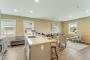 Una cocina moderna con una isla central, un área de comedor con un sofá y vistas al exterior a través de amplias ventanas.