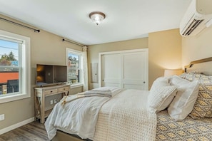 A bedroom with a bed, a desk, a television, and a window.