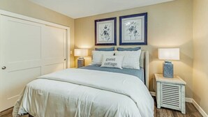 A bedroom with a bed, two bedside tables with lamps, a door, and two framed floral pictures on the wall. - Front Street Suite Poulsbo (Poulsbo)