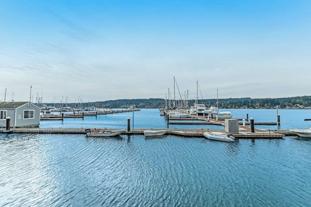 A marina with boats docked at piers, a small building, and calm water under a clear sky.