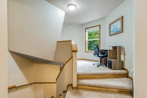 Een trap die leidt naar een kamer met een bureau, stoel en een raam met uitzicht op groen.